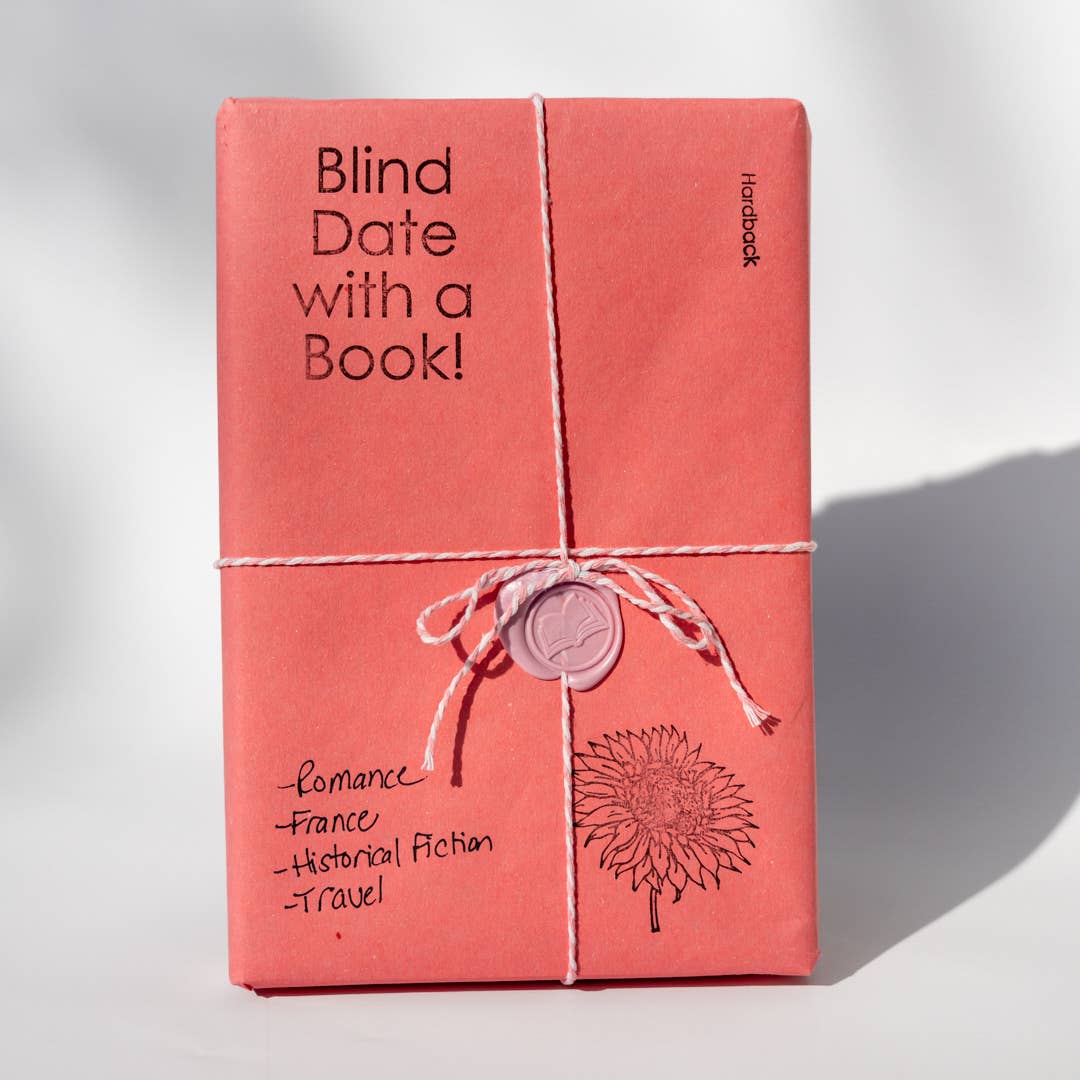 A pink-wrapped book with 'Blind Date with a Book' written on it, tied with twine and featuring a stamp and illustrations on the wrapping.